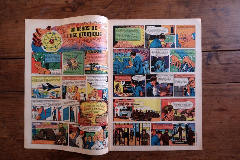 May include: Open comic book pages featuring colorful panels from a vintage comic. The title "UN HEROS DE L'AGE ATOMIQUE" is visible. The panels depict scenes with people, explosions, and a jet plane, all in a retro style.