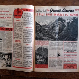 May include: An open vintage magazine with French text and illustrations. Headlines include "Le Tour du Monde" and "Le Plus Haut Barrage du Monde." The pages are on a wooden surface.