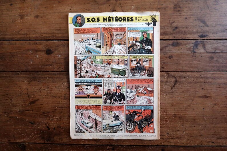 Peut inclure: Une page de bande dessin&eacute;e vintage intitul&eacute;e S.O.S. METEORES par E.P. Jacobs, compos&eacute;e d'une grille de vignettes color&eacute;es illustrant des sc&egrave;nes enneig&eacute;es, des v&eacute;hicules et des personnages en action, avec des bulles de texte en fran&ccedil;ais.