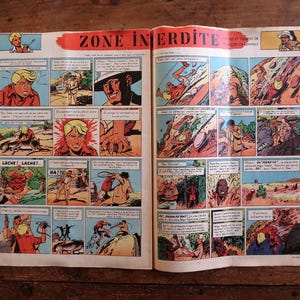 Peut inclure: Une double page de bande dessin&eacute;e vintage intitul&eacute;e ZONE INTERDITE, compos&eacute;e de vignettes color&eacute;es illustrant des sc&egrave;nes d'action avec des personnages, dont une personne blonde en chemise rouge, des paysages d&eacute;sertiques et des bulles de texte.