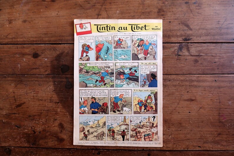 May include: A vintage comic book titled "Tintin au Tibet" in French, featuring colorful panels depicting adventure scenes. The cover has a red and white logo and is set against a wooden background.
