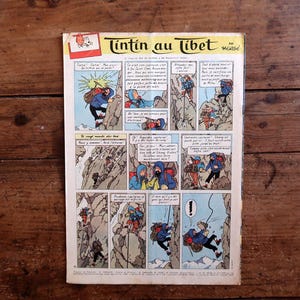 Puede incluir: Un c&oacute;mic vintage titulado "Tint&iacute;n en el T&iacute;bet" en franc&eacute;s, con paneles coloridos que representan escenas de escalada de monta&ntilde;a. La portada tiene un logotipo rojo y blanco. El c&oacute;mic est&aacute; sobre una superficie de madera.