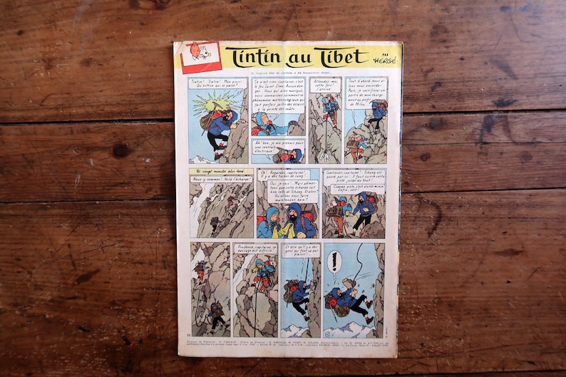 Puede incluir: Un c&oacute;mic vintage titulado "Tint&iacute;n en el T&iacute;bet" en franc&eacute;s, con paneles coloridos que representan escenas de escalada de monta&ntilde;a. La portada tiene un logotipo rojo y blanco. El c&oacute;mic est&aacute; sobre una superficie de madera.