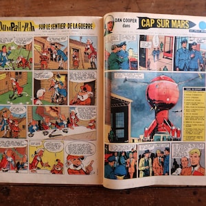 May include: An open vintage comic book featuring two distinct stories. The left page displays Oumpah-Pah sur le sentier de la guerre with colorful panels. The right page shows Dan Cooper dans Cap sur Mars, featuring a large red spherical spacecraft.