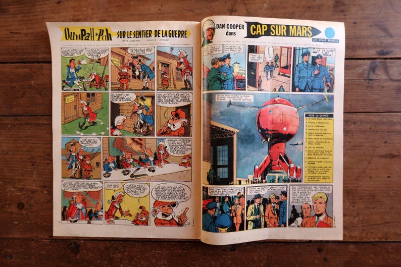 May include: An open vintage comic book featuring two distinct stories. The left page displays Oumpah-Pah sur le sentier de la guerre with colorful panels. The right page shows Dan Cooper dans Cap sur Mars, featuring a large red spherical spacecraft.