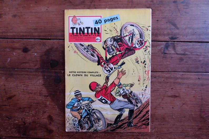 May include: Vintage comic book cover featuring a motorcycle race scene with riders in action. The cover has the title "TINTIN" and the text "40 pages". The comic book is on a wooden surface.