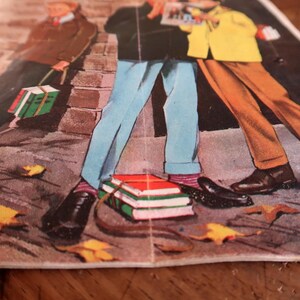 Peut inclure: Une illustration de style vintage imprim&eacute;e sur papier repr&eacute;sentant trois personnages debout sur un trottoir avec des feuilles d'automne &eacute;parpill&eacute;es. Les personnages portent des pantalons bleu clair, marron et gris fonc&eacute;, avec des piles de livres.