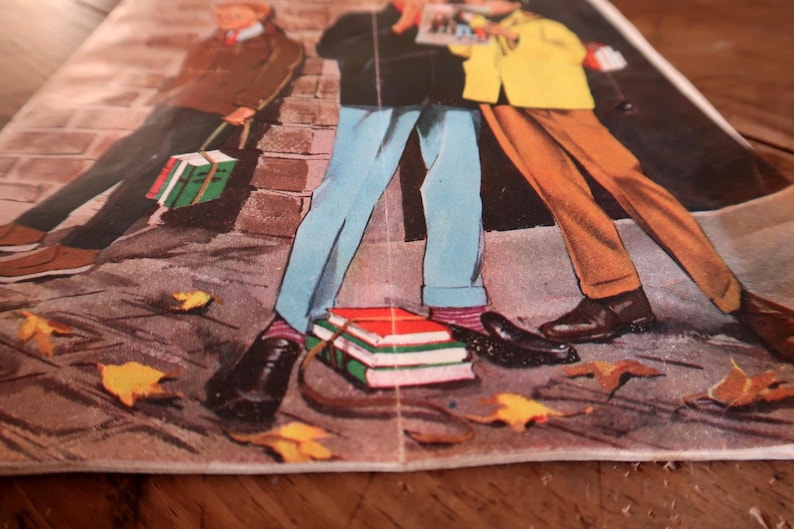 Peut inclure: Une illustration de style vintage imprim&eacute;e sur papier repr&eacute;sentant trois personnages debout sur un trottoir avec des feuilles d'automne &eacute;parpill&eacute;es. Les personnages portent des pantalons bleu clair, marron et gris fonc&eacute;, avec des piles de livres.