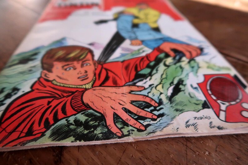 May include: A vintage comic book cover depicting a dramatic scene of a person in a red jacket reaching out, with another figure in blue and yellow. The artwork is in a classic comic book style, with bold colours and dynamic poses.