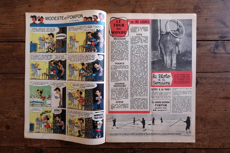 May include: Open vintage magazine spread featuring comic strips and articles. The left page displays a comic with speech bubbles. The right page has text and a photo of an elephant with a ring. The magazine is on a wooden surface.