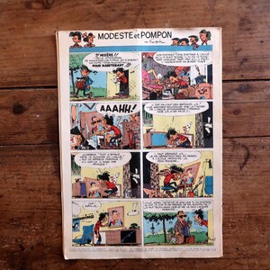 May include: A vintage comic book page titled Modeste et Pompon featuring a multi-panel grid with colorful illustrations and French text. The paper has visible aging, including yellowing edges and a central horizontal crease on the rectangular sheet.