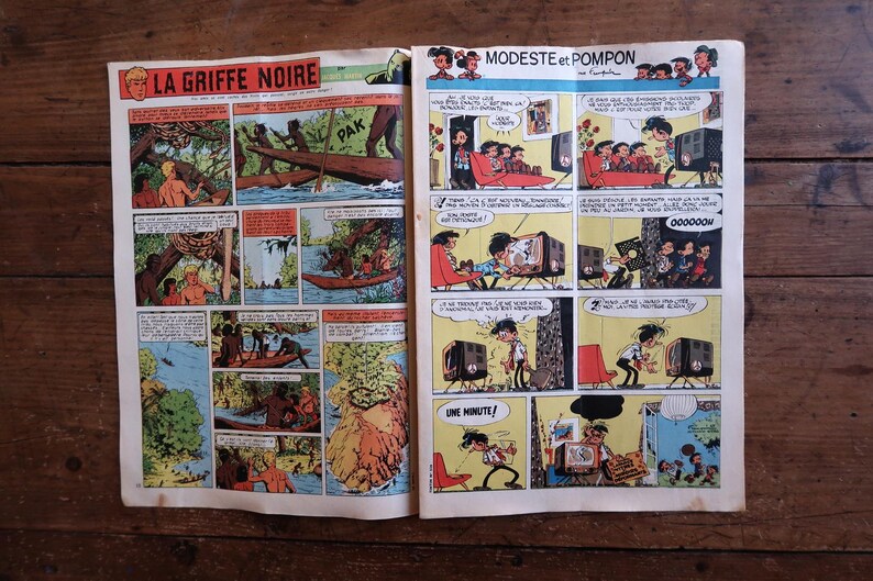 Peut inclure: Une double page de bande dessin&eacute;e vintage pr&eacute;sentant deux histoires distinctes. La page de gauche est intitul&eacute;e LA GRIFFE NOIRE et illustre des sc&egrave;nes de jungle avec des pirogues. La page de droite, MODESTE et POMPON, montre des personnages.