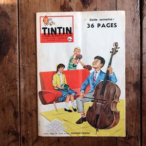 May include: Vintage "Tintin" comic book cover featuring a boy playing a cello, with other children and text. The cover has a red and white logo and text that reads "36 PAGES". The comic is on a wooden surface.