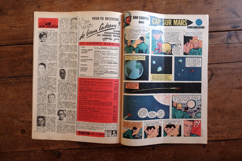 May include: Open vintage comic book pages with French text and illustrations. The right page features a space-themed comic strip titled "CAP SUR MARS." The left page has text and small portraits. The book is open on a wooden surface.