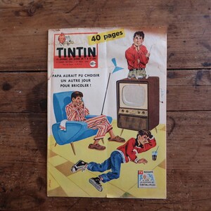 May include: A vintage Tintin magazine cover featuring a yellow background with a blue armchair, a brown television set, and two figures. The text reads TINTIN, 40 pages, and PAPA AURAIT PU CHOISIR UN AUTRE JOUR POUR BRICOLER. The cover art shows a person in striped pajamas and another in a red sweater and blue jeans.