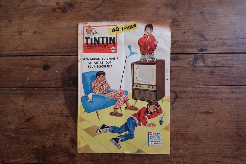 May include: A vintage Tintin magazine cover featuring a yellow background with a blue armchair, a brown television set, and two figures. The text reads TINTIN, 40 pages, and PAPA AURAIT PU CHOISIR UN AUTRE JOUR POUR BRICOLER. The cover art shows a person in striped pajamas and another in a red sweater and blue jeans.