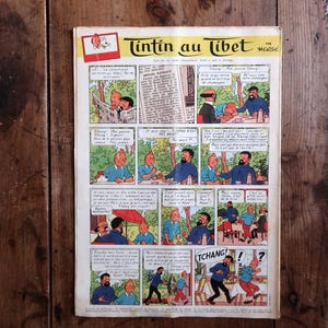 May include: A vintage comic book page titled "Tintin au Tibet" featuring a series of illustrated panels. The panels depict scenes with characters in various settings, with speech bubbles containing text. The comic is set against a wooden background.