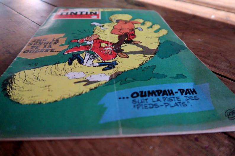 May include: A vintage Tintin comic book titled Sur le sentier de la guerre featuring a green cover with a large yellow footprint illustration. The artwork depicts a character in a red coat and a figure in brown clothing with the text Oumpah-pah.