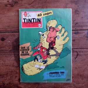 May include: A vintage Tintin comic book with a green cover featuring a large yellow footprint illustration. The cover displays the text Tintin, 40 pages, Sur le sentier de la guerre, and Oumpah-pah suit la piste des pieds-plats with cartoon characters.