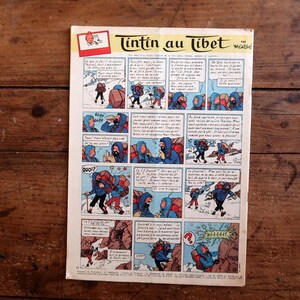 May include: A vintage comic book page titled "Tintin in Tibet" featuring a series of illustrated panels. The panels depict characters in winter clothing, navigating snowy terrain. The comic is set against a wooden background.