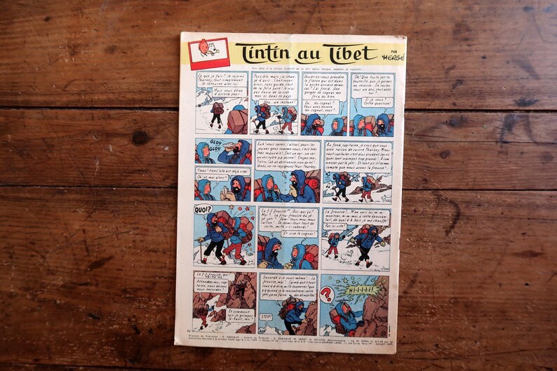 May include: A vintage comic book page titled "Tintin in Tibet" featuring a series of illustrated panels. The panels depict characters in winter clothing, navigating snowy terrain. The comic is set against a wooden background.