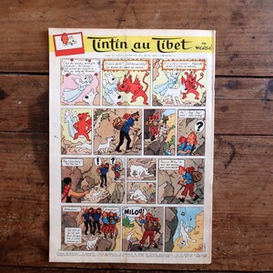 May include: A vintage comic book page titled "Tintin in Tibet" featuring colorful panels. The artwork depicts characters in various scenes, including a man with a dog, and fantastical creatures. The comic is set against a wooden background.