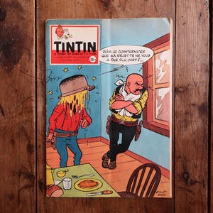 May include: Vintage comic book cover featuring the character Tintin. The cover art depicts two cartoon figures in a room, one with a hat and the other with a stern expression. Text includes "TINTIN" and a speech bubble.