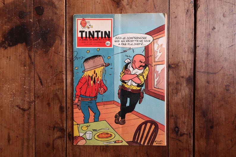 May include: Vintage comic book cover featuring the character Tintin. The cover art depicts two cartoon figures in a room, one with a hat and the other with a stern expression. Text includes "TINTIN" and a speech bubble.