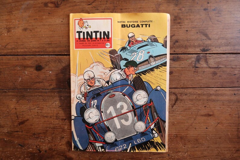 May include: A vintage Tintin comic magazine with a yellow cover featuring a blue Bugatti race car numbered 13 in the foreground and a light blue race car numbered 28 in the background. The text reads Tintin, Notre Histoire Complete: Bugatti.