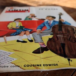 May include: Vintage comic book cover featuring a cartoon illustration. The cover shows a man playing a cello, a woman reading, and the text "TINTIN". The background is yellow with the text "COUSINE EDWIGE".