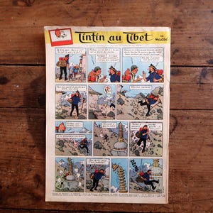 May include: A vintage comic book page titled Tintin au Tibet featuring a multi-panel color illustration. The comic strip depicts characters in a mountainous landscape with dialogue bubbles in French. The paper has a cream background with aged edges.