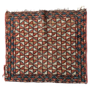 May include: Square, hand-woven rug with a repeating geometric pattern in shades of red, blue, beige, and black. The rug has a detailed border with a triangular design. The edges of the rug are frayed, giving it a vintage appearance.