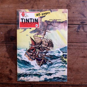 May include: A vintage comic book cover featuring a sailing ship battling rough seas. The cover has the title "TINTIN" in red and white, with the text "40 pages" in a yellow banner. The background is a wooden surface.