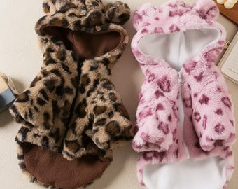 May include: Two plush dog coats. One is brown with black spots, the other is pink with darker pink spots. Both have hoods with bear ears and a zipper closure. The coats are designed to keep small dogs warm and stylish.