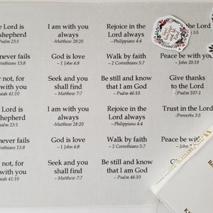 Może przedstawiać: Biała Biblia z czerwonymi literami oraz kolekcja naklejek i cytatów z Biblii. Cytaty są wydrukowane na białym tle czarnym tekstem. Naklejki mają kwiatowe wzory.