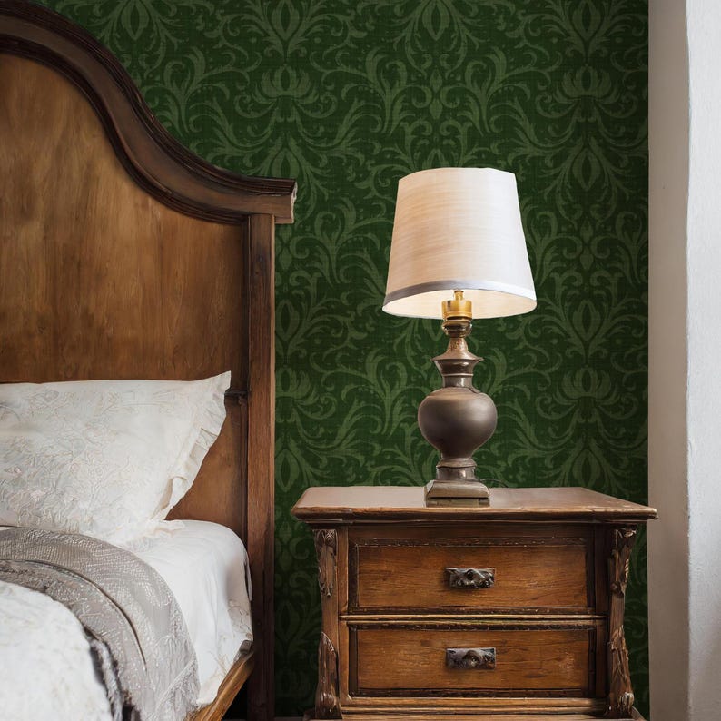 May include: A bedroom scene featuring a wooden bed frame, a nightstand, and a lamp. The nightstand has two drawers and a decorative design. The lamp has a beige lampshade and a dark brown base. The wall is covered in a green floral wallpaper.