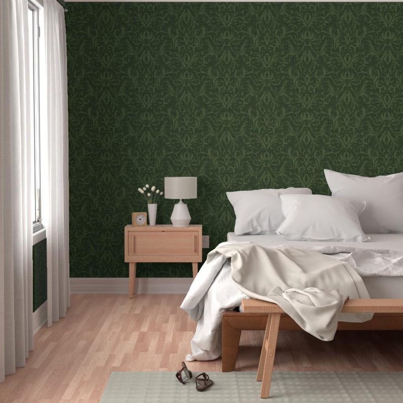 May include: A bedroom with a green damask patterned wallpaper, a wooden bench, and a bed with white bedding. A small wooden nightstand with a lamp and a vase of flowers sits next to the bed. The room has a light wood floor and a window with white curtains.