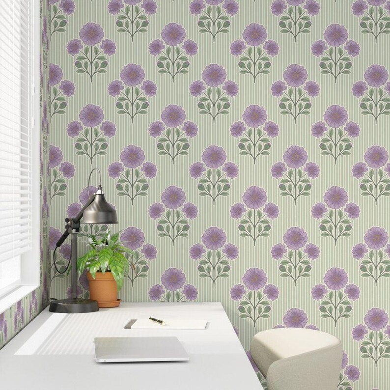 May include: A desk with a laptop, a notebook, and a pen sits against a wall covered in light green wallpaper featuring a repeating pattern of purple flowers and green leaves with thin vertical stripes throughout the design.
