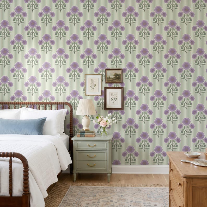 May include: A bedroom scene featuring wallpaper with a repeating pattern of purple flowers and green leaves on a light green striped background. A bed with white bedding and a blue pillow sits next to a light green nightstand with two framed prints.