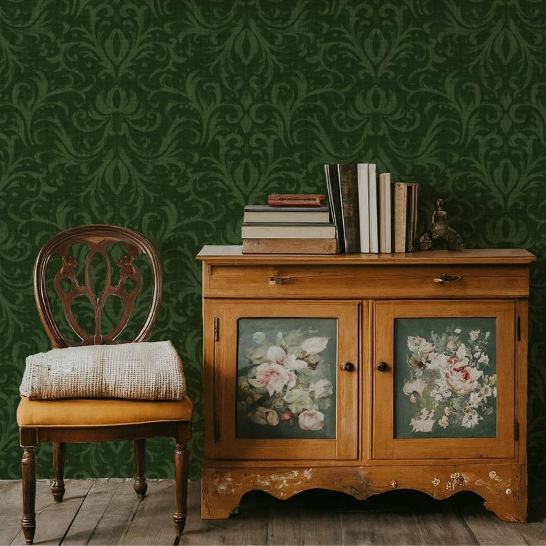 May include: A vintage wooden cabinet with floral painted glass doors, topped with books and a small statue. A wooden chair with a yellow cushion and a blanket sits in front of a dark green patterned wall. The scene evokes a classic, antique aesthetic.