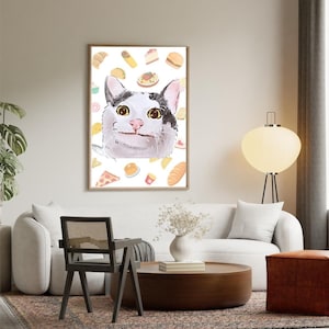 May include: A framed watercolor print featuring a cat with a surprised expression, surrounded by illustrations of various foods like pizza, tacos, and pastries. The cat has black and white markings and large yellow eyes. The print is displayed in a living room setting.
