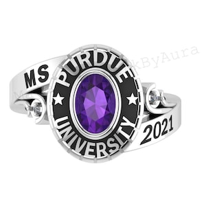 May include: A silver ring featuring a large oval purple gemstone at the center. The ring has the words "PURDUE UNIVERSITY" and "2021" engraved on it. The ring also has the initials "MS" on it.
