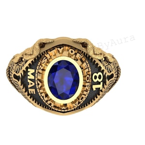 May include: Gold-toned ring with a large, oval blue gemstone. The ring features the text "UNIVERSITY OF FLORIDA" and "MAE 18". Two detailed dragon-like figures adorn the sides of the ring.