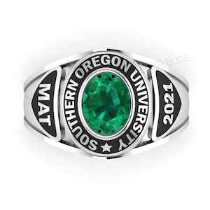 May include: A silver-colored class ring with a large, oval-cut, emerald-green gemstone at the center. The ring features the words "SOUTHERN OREGON UNIVERSITY" and "2021" in black lettering. The ring also has the letters "MAT" on the side.