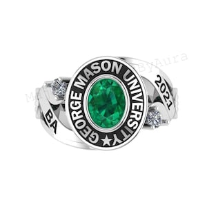 May include: A silver ring featuring a large oval emerald-green stone at the center, surrounded by the words "GEORGE MASON UNIVERSITY" in black. The ring also has the year "2021" and two smaller clear stones. The ring is a graduation ring.