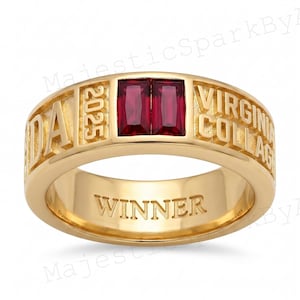 May include: A gold-colored ring with the words "DA" and "VIRGINIA COLLEGE" engraved on the band. The ring features two rectangular, deep red gemstones and the year "2025". The word "WINNER" is also engraved on the ring.