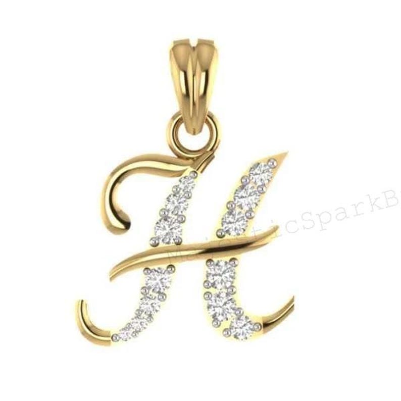 May include: A gold pendant shaped like the letter H in a cursive script font. The letter features a polished gold finish on the left side and a series of small, round, clear, sparkling stones embedded along the right side of the letter form.