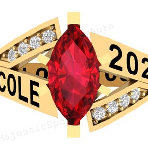 May include: A gold ring with a central, red, marquise-cut gemstone. The ring is inscribed with the name "NICOLE" and the year "2020" in black. Each side features a row of small, clear gemstones.