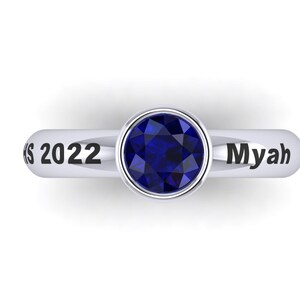 May include: A silver ring featuring a deep blue gemstone. The ring is inscribed with "Class 2022" and the name "Myah". The ring is set against a white backdrop.