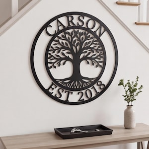 May include: A circular black metal wall sign featuring a tree of life silhouette in the centre. The name CARSON is arched across the top, and the text EST 2018 is positioned along the bottom curve within the circular frame design.